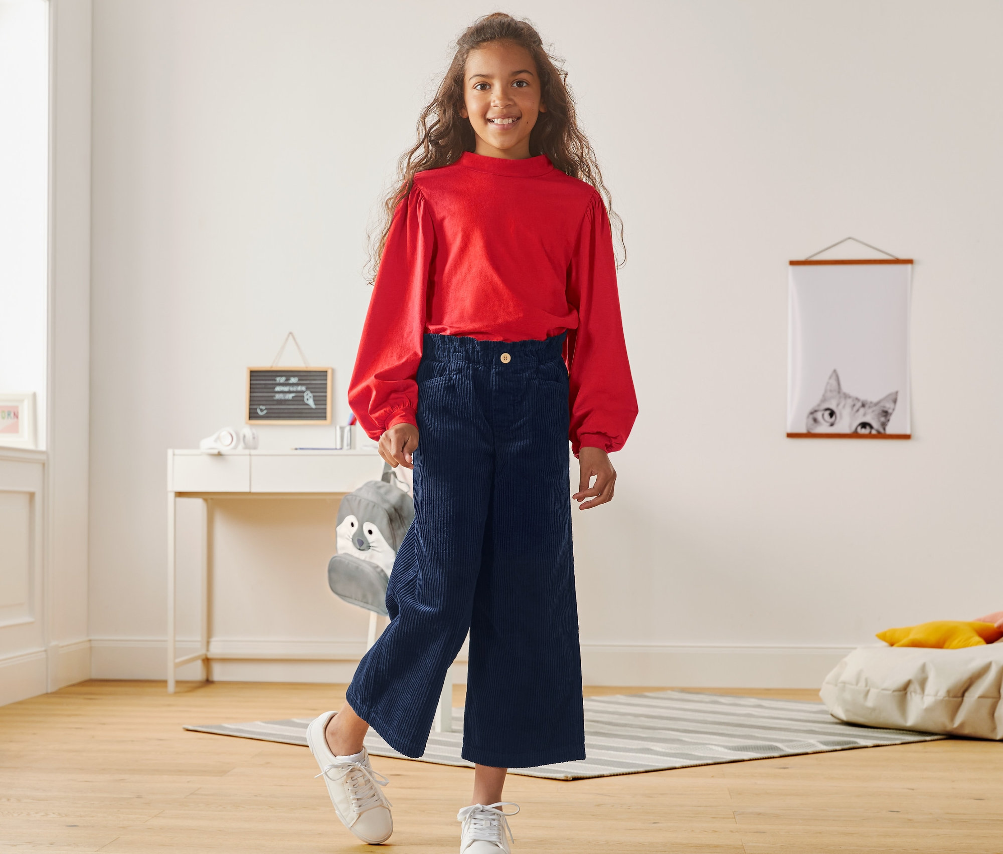 Dziewczyna pozuje w czerwonym topie i sztruksowych kulotach.