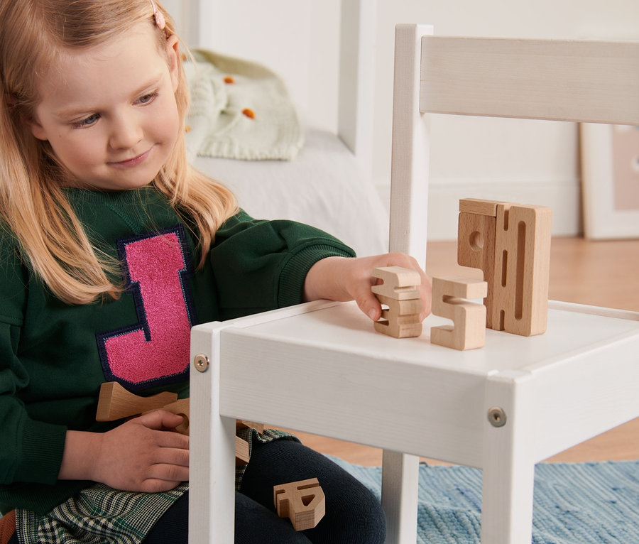 Dziewczynka bawi się klockami z cyframi na białym krześle.