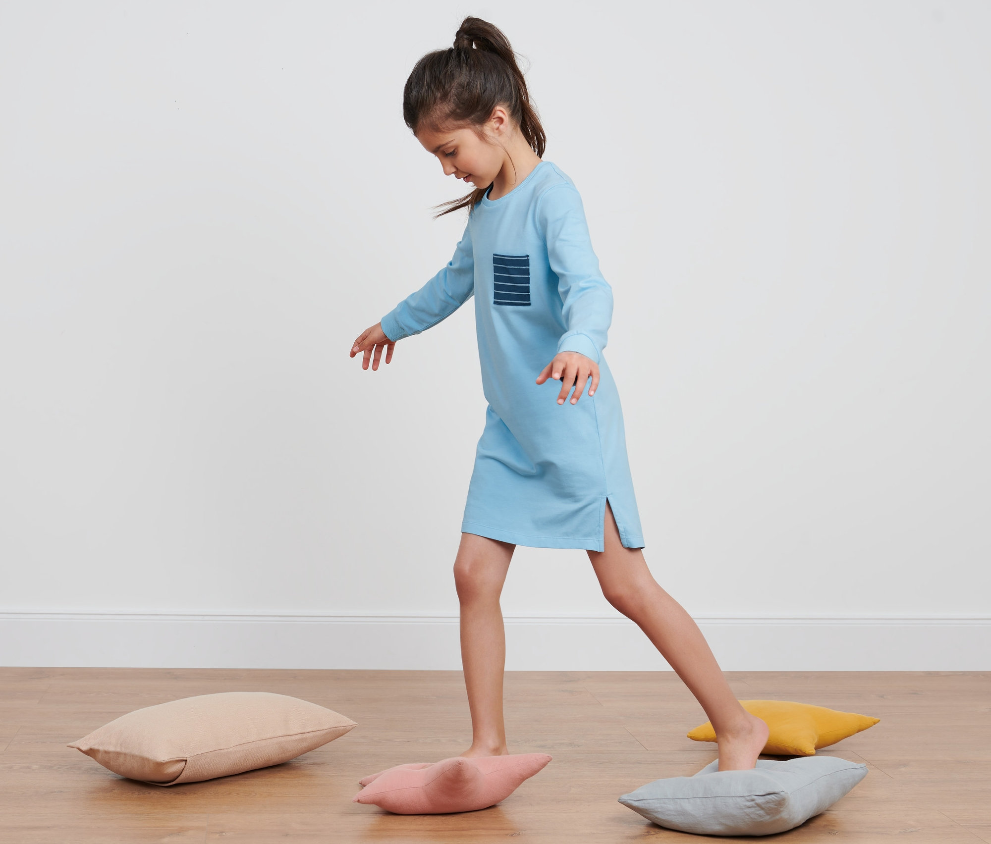 Dziewczyna w dziewczęcej koszuli nocnej balansuje na poduszkach.