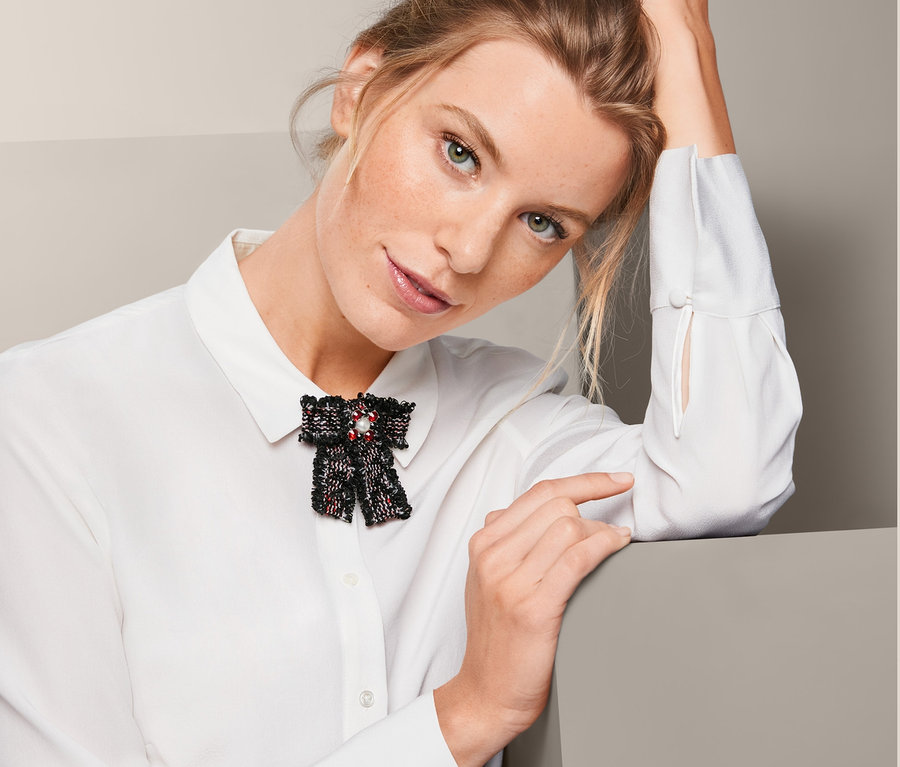 Kobieta z broszką w kształcie kokardki z tweedu na białej koszuli.