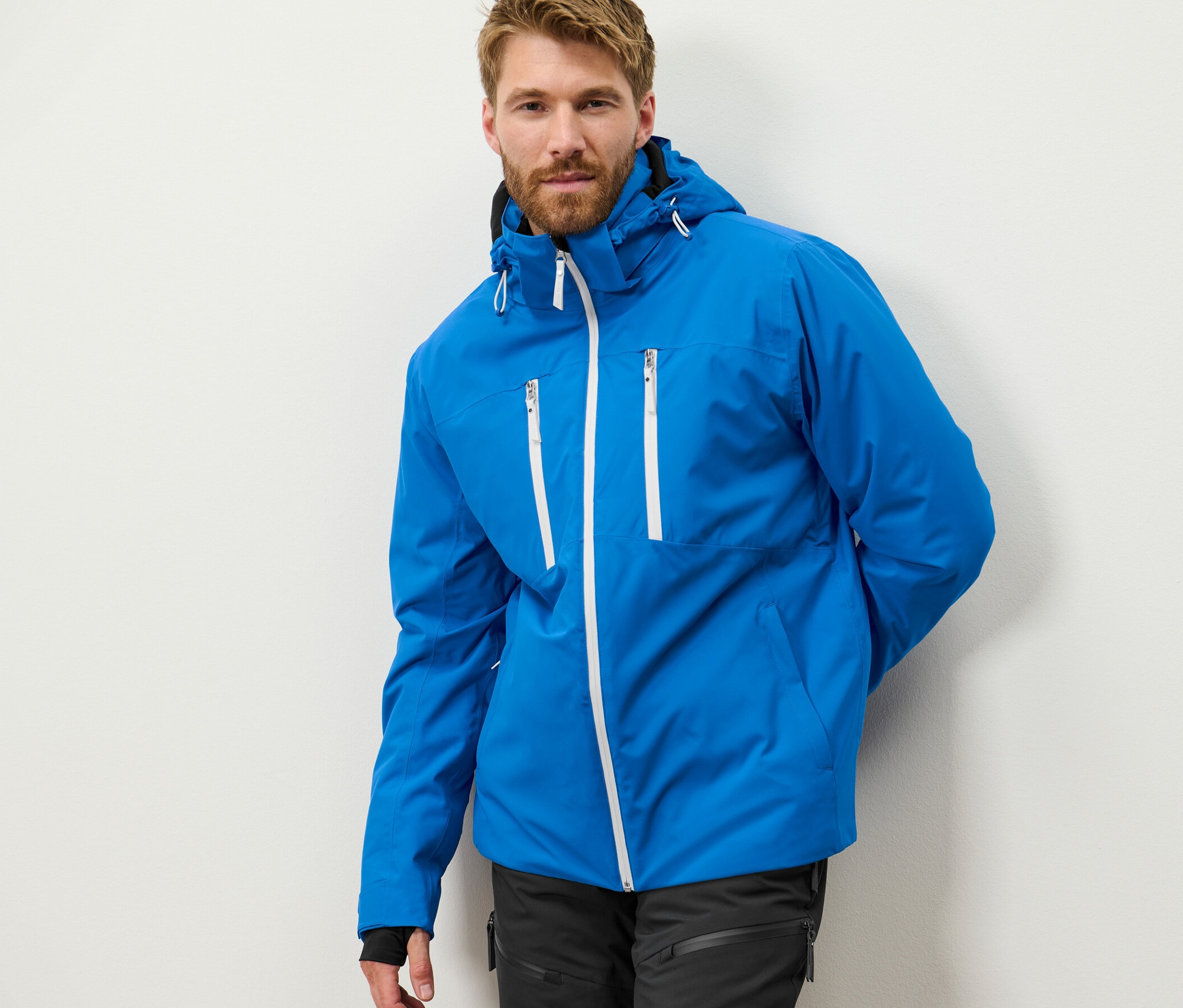 Mężczyzna z brodą pozuje w niebieskiej, profesjonalnej kurtce narciarskiej.