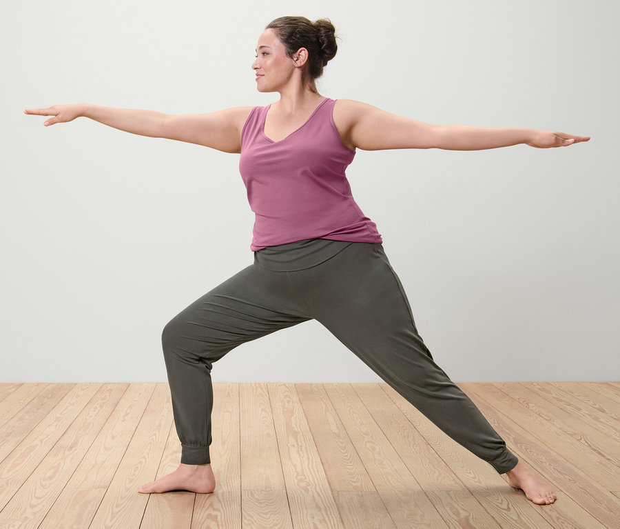 Kobieta w pozycji wojownika w liliowym topie (2 sztuki) i spodniach do jogi.