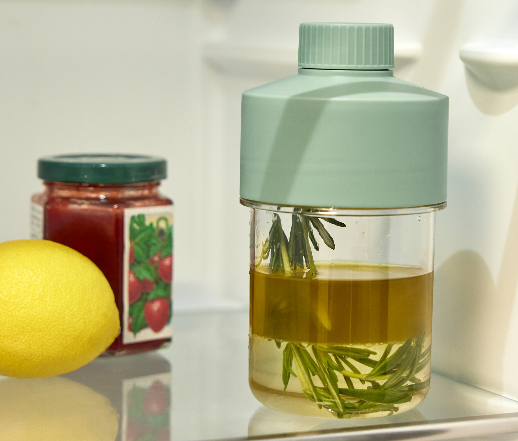 W lodówce stoi butelka na dressing, słoik dżemu i cytryna.