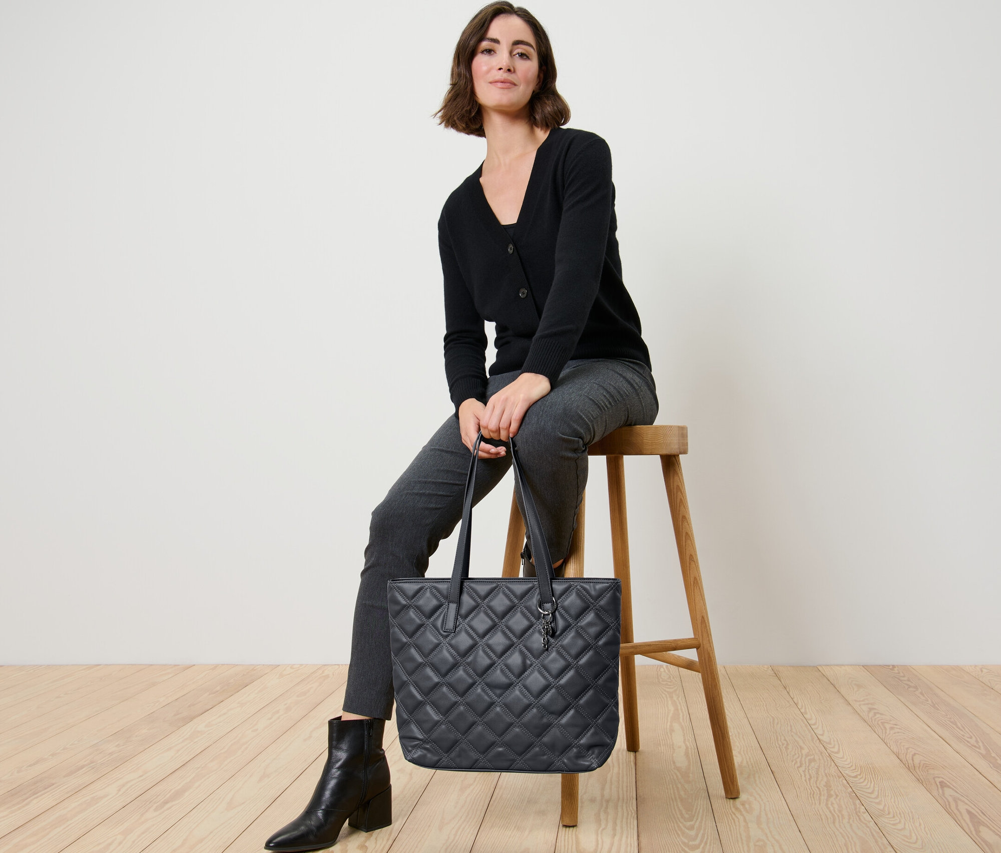 Kobieta siedzi na stołku i trzyma torbę shopperkę.