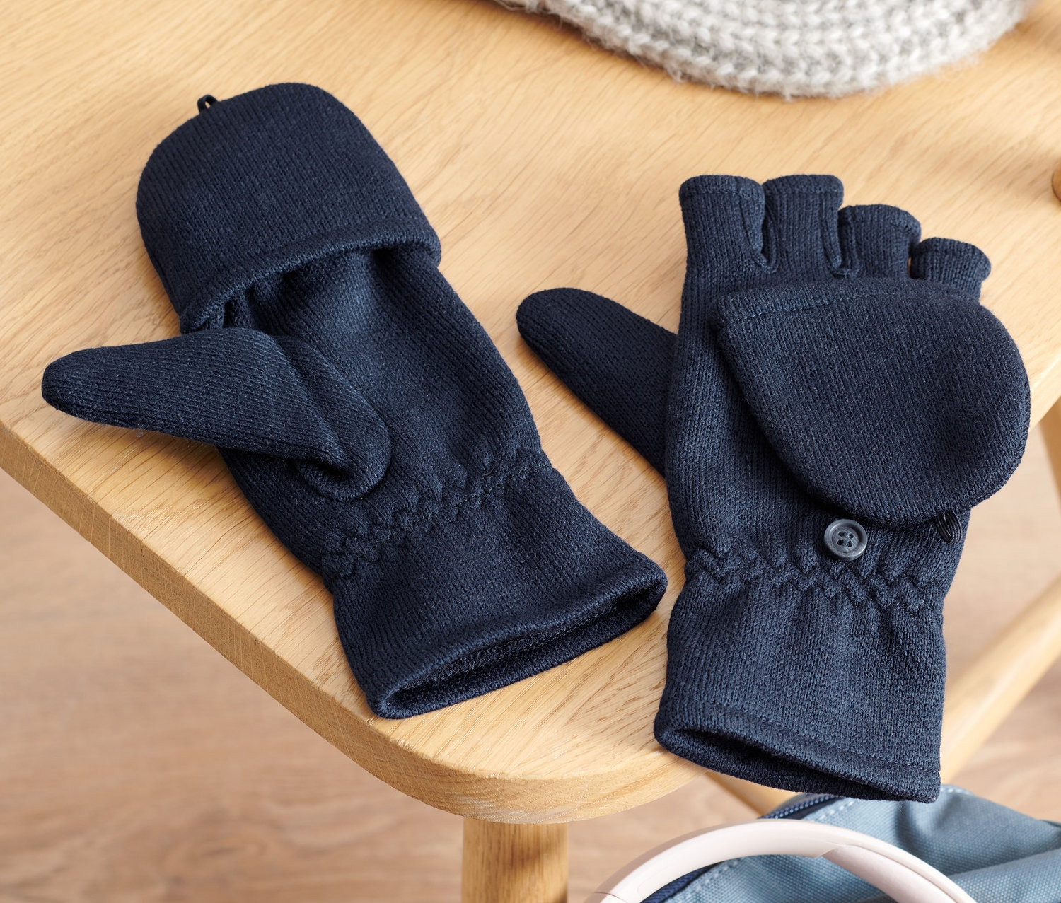 Na drewnianym krześle leżą rękawiczki polarowe z klapką, dzianinowa czapka i słuchawki na plecaku.