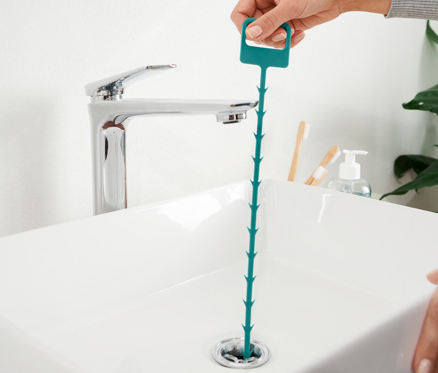 Ręka wkłada czyścik do odpływu umywalki.