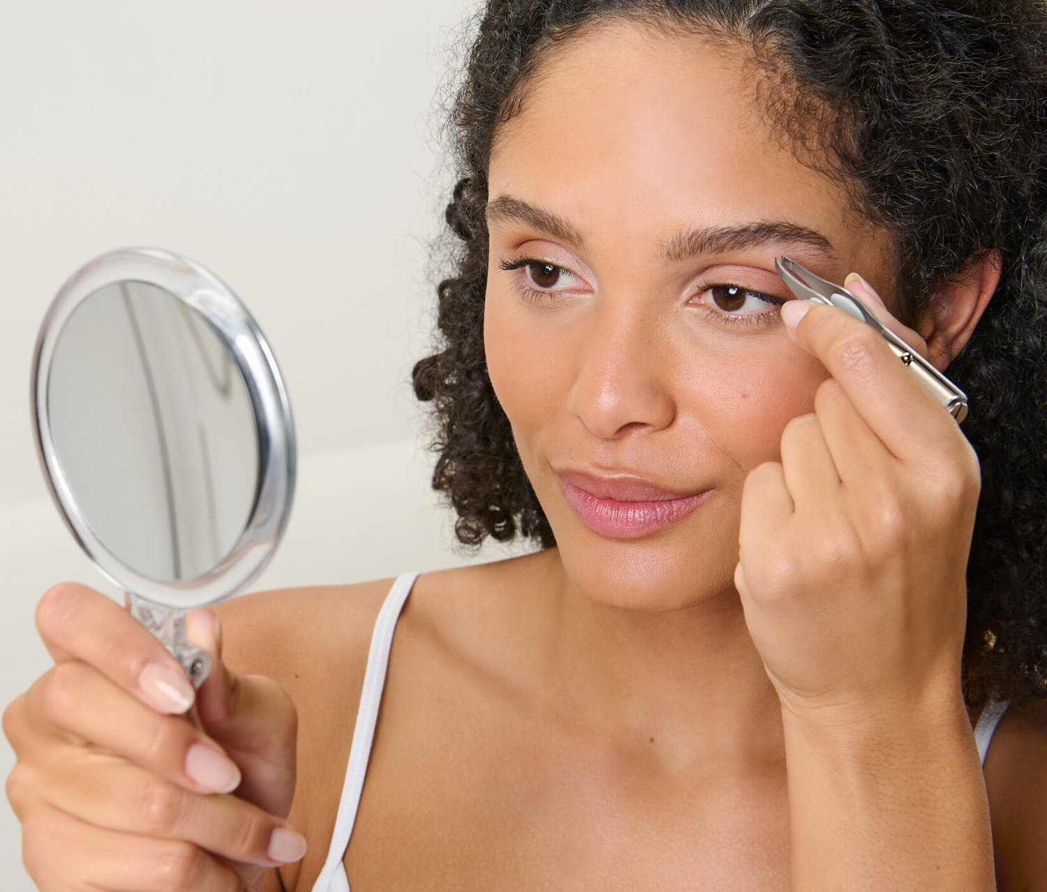 Kobieta reguluje brwi pęsetą z podświetleniem LED, patrząc w lusterko.