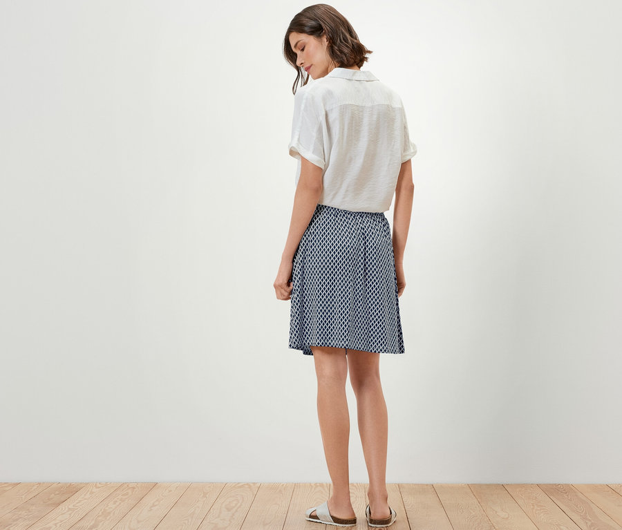 Kobieta stoi tyłem do aparatu, ubrana w top i spódnicę z dżerseju z nadrukiem.