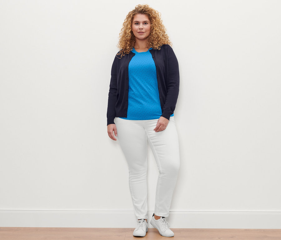 Kobieta pozuje w T-shircie w kropki, kremowobiałych spodniach dżinsowych »Fit Emma« i kardiganie z delikatnej dzianiny.