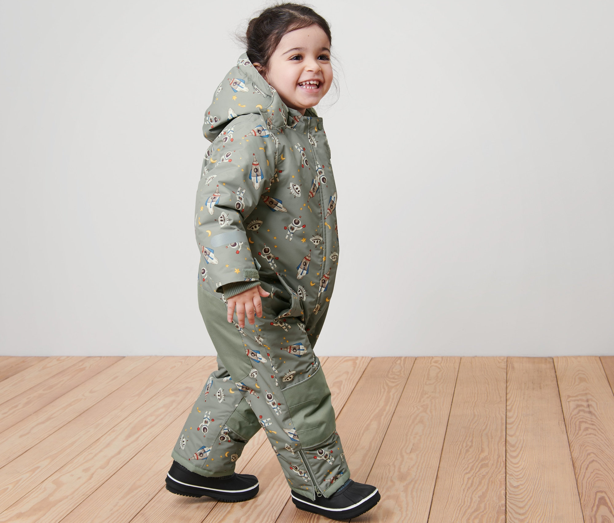 Uśmiechnięte dziecko idzie, ubrane w dziecięcy kombinezon zimowy z nadrukiem kosmosu.