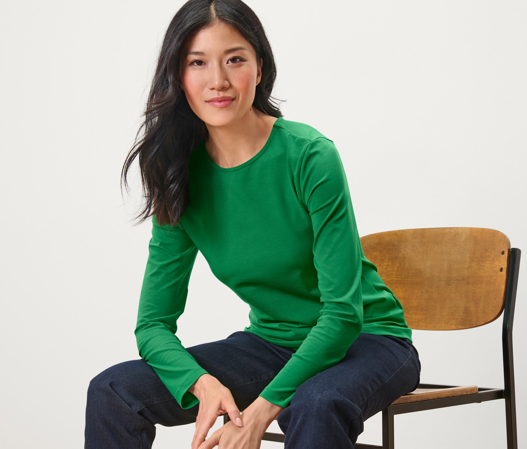 Kobieta siedzi na krześle i ma na sobie zieloną koszulkę z długim rękawem.