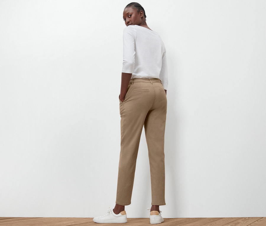 Kobieta pozuje tyłem do aparatu, ubrana w beżowe spodnie chinosy.