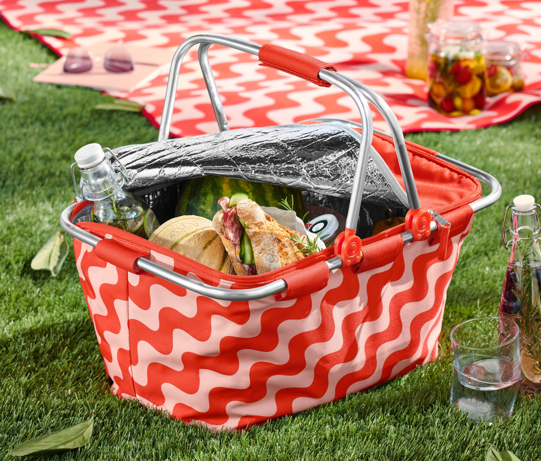Na trawie stoi koszyk termiczny z jedzeniem i piciem.