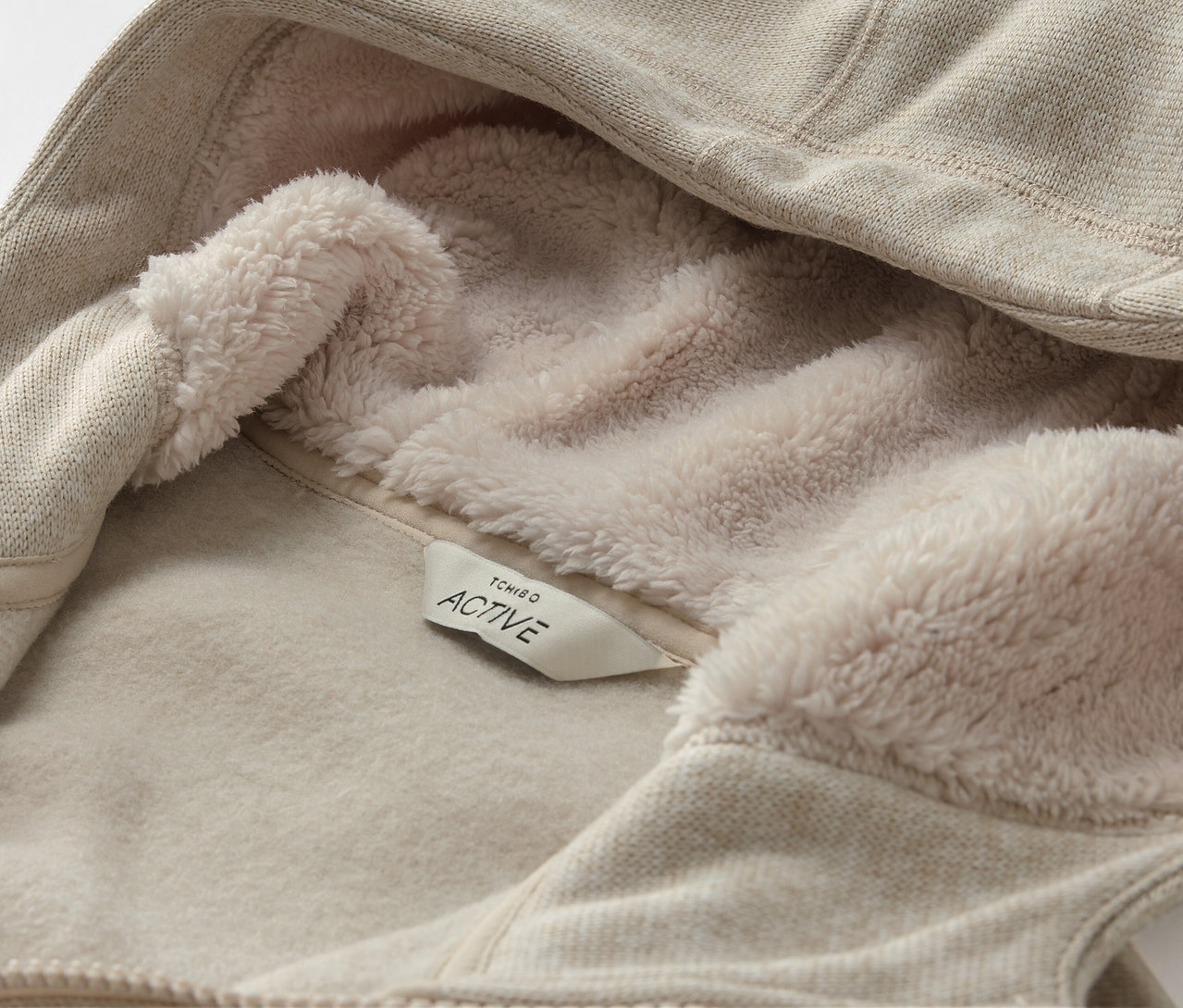 Zbliżenie beżowej bluzy z kapturem, z polarową podszewką i metką ACTIVE.