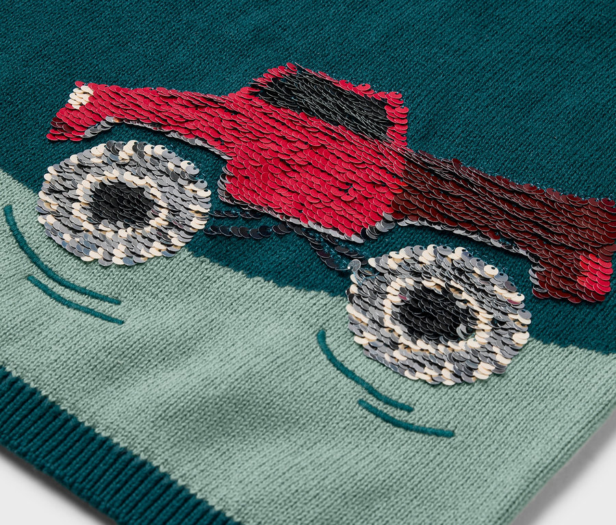 Zbliżenie na dziergany sweter dziecięcy z naszywką czerwonego monster trucka.