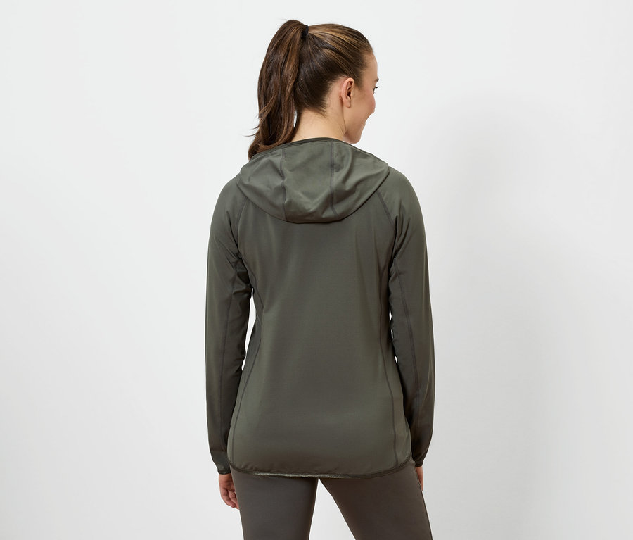 Kobieta z brązowymi włosami związanymi w kucyk ma na sobie oliwkową kurtkę z kapturem i oliwkowe legginsy.