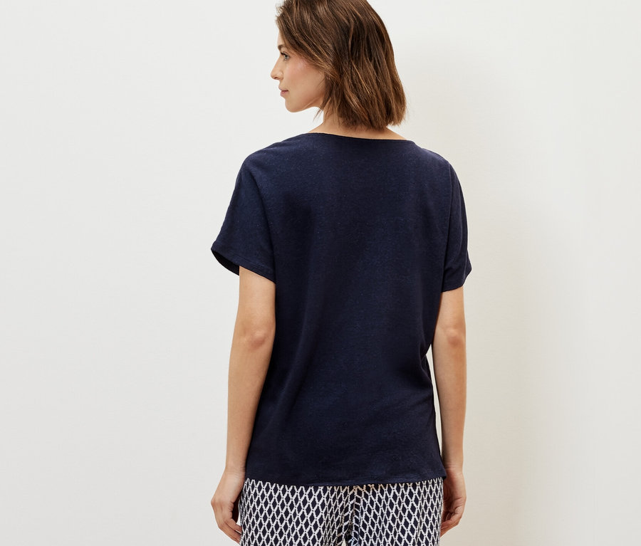 Kobieta ma na sobie granatową bluzkę z zawartością lnu i wzorzyste spodnie.