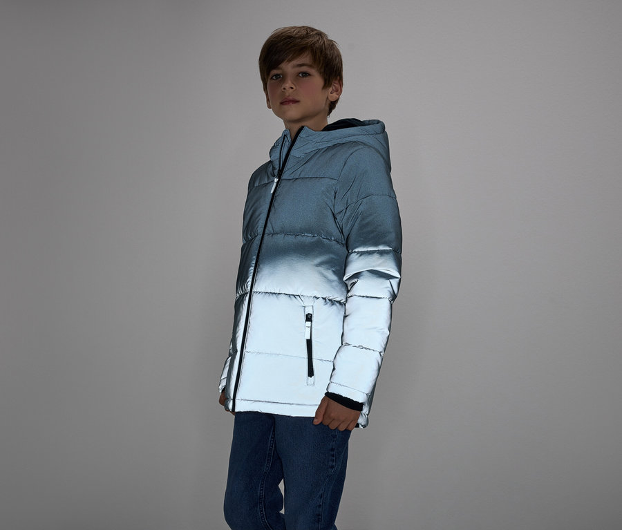 Chłopiec w niebieskiej kurtce puchowej i dżinsach stoi na szarym tle.