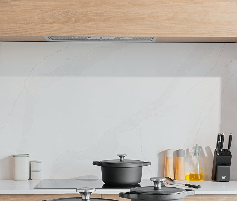 Trzy czarne garnki z pokrywkami na białym blacie kuchennym. Na desce do krojenia leżą pomidory i ziemniaki.