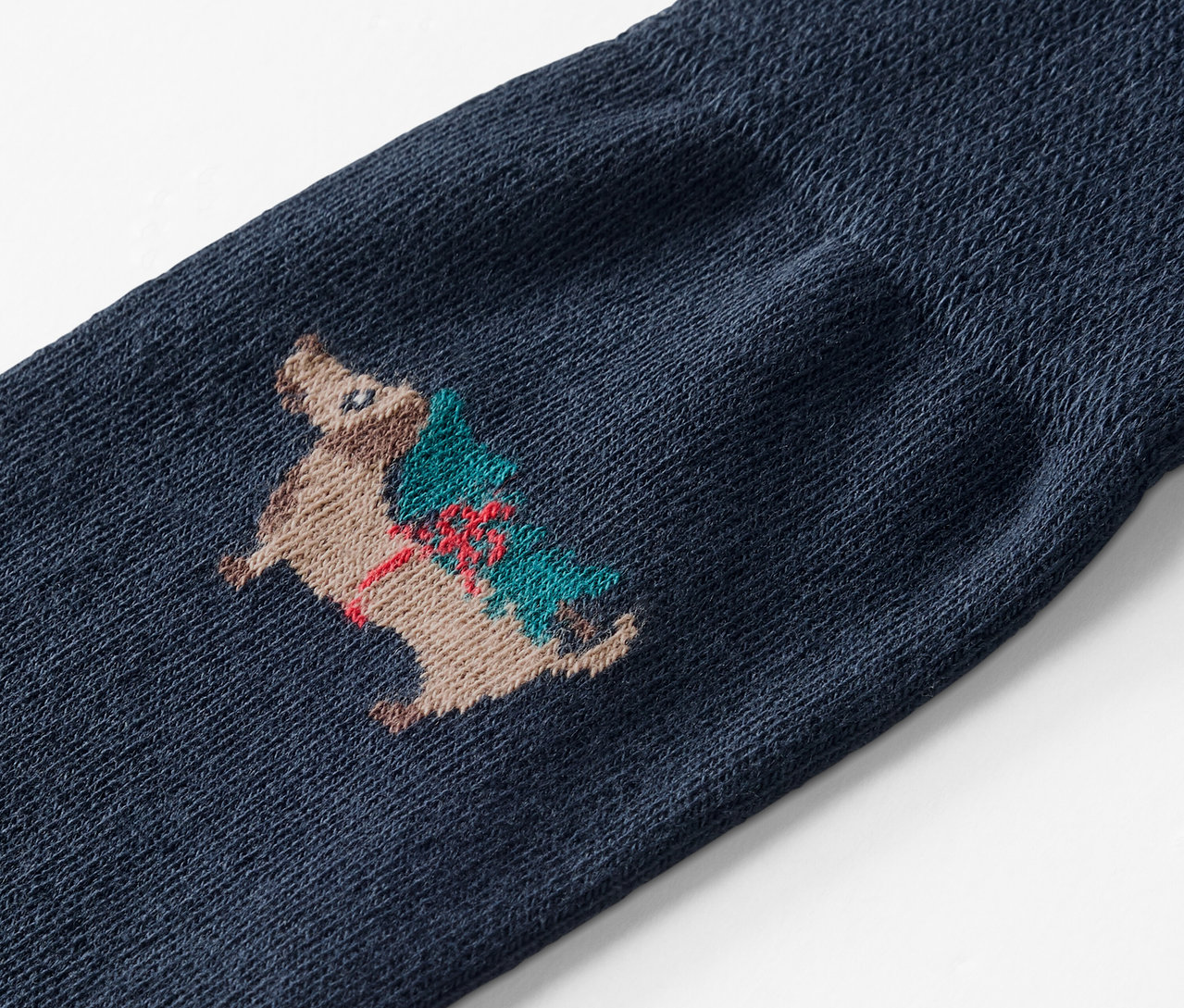 Zbliżenie na niebieską skarpetę z haftem jeża niosącego choinkę.