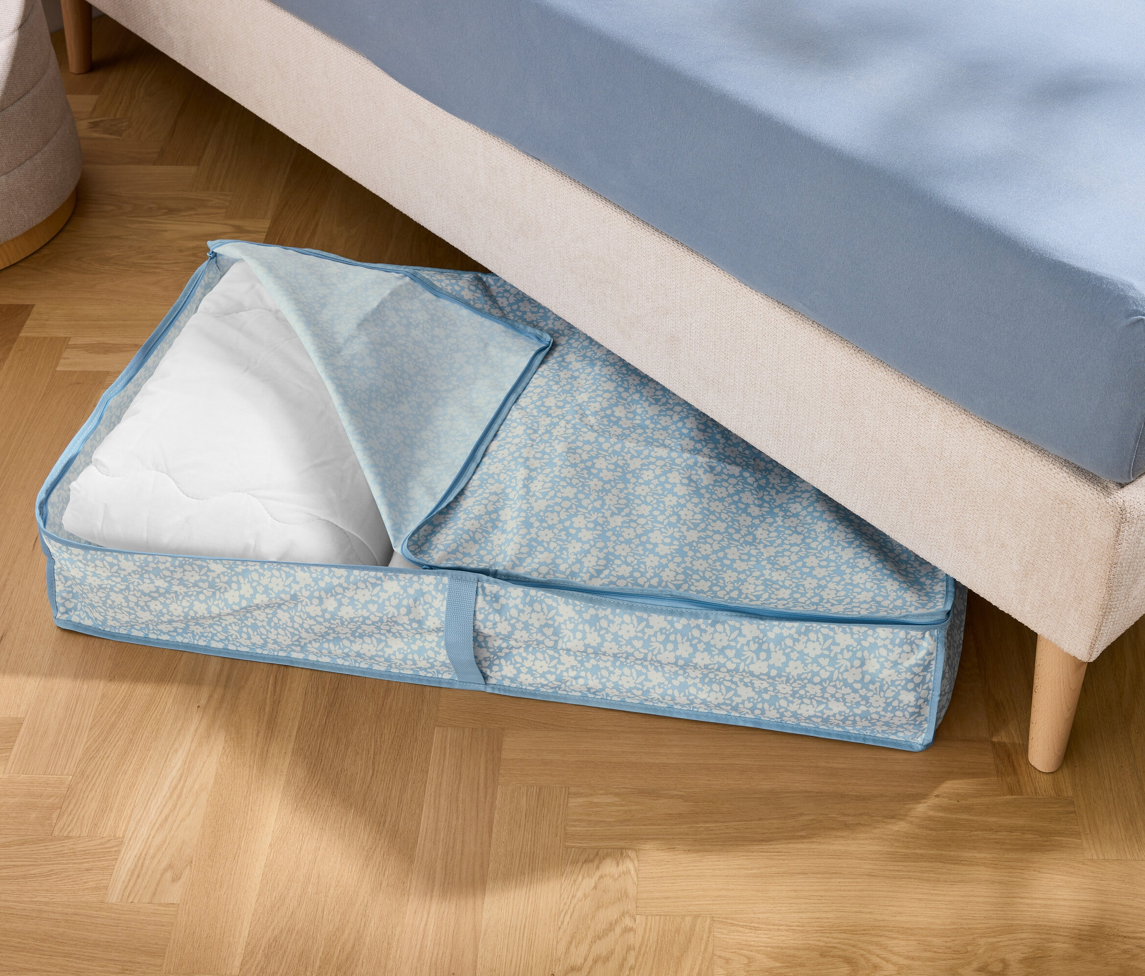 Pod łóżkiem leży niebieska torba do przechowywania z białym wypełnieniem.