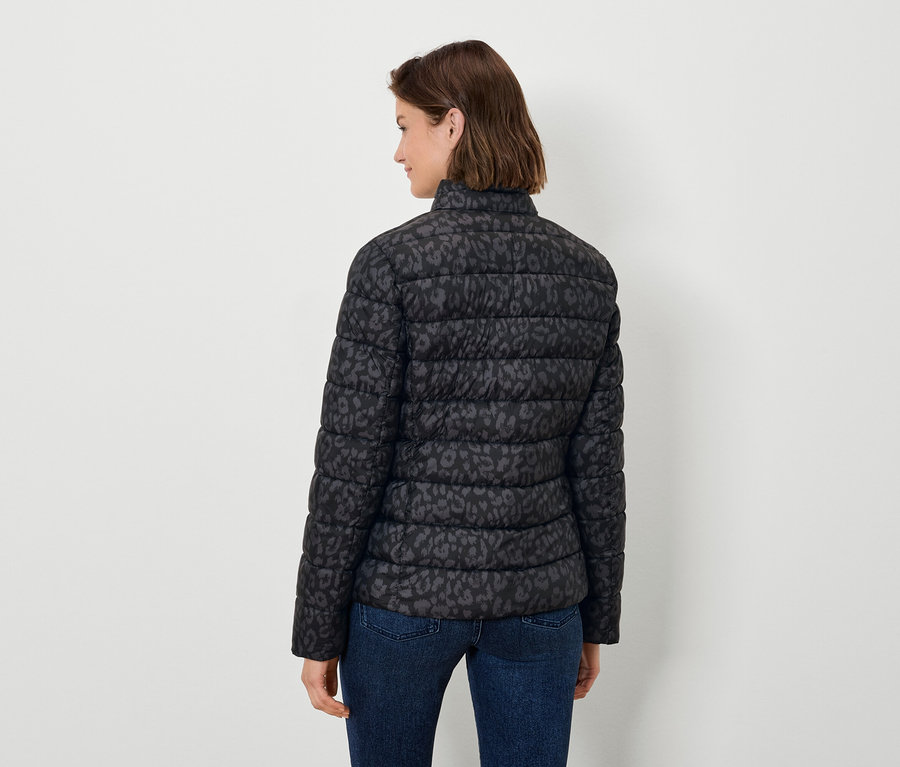 Kobieta tyłem do kamery ma na sobie czarną, pikowaną kurtkę w zwierzęcy wzór i dżinsy.