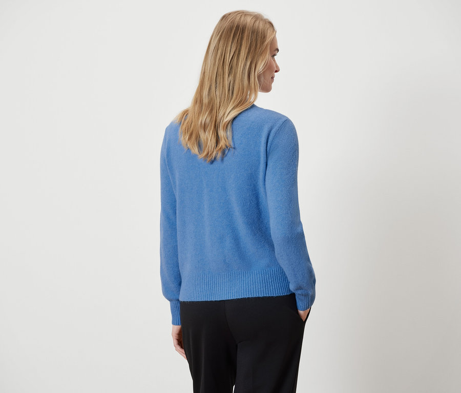 Na zdjęciu kobieta widziana od tyłu, ubrana w niebieski sweter i czarne spodnie.