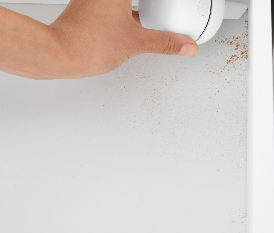 Ręka trzyma biały, kulisty środek czyszczący w białej szafce.