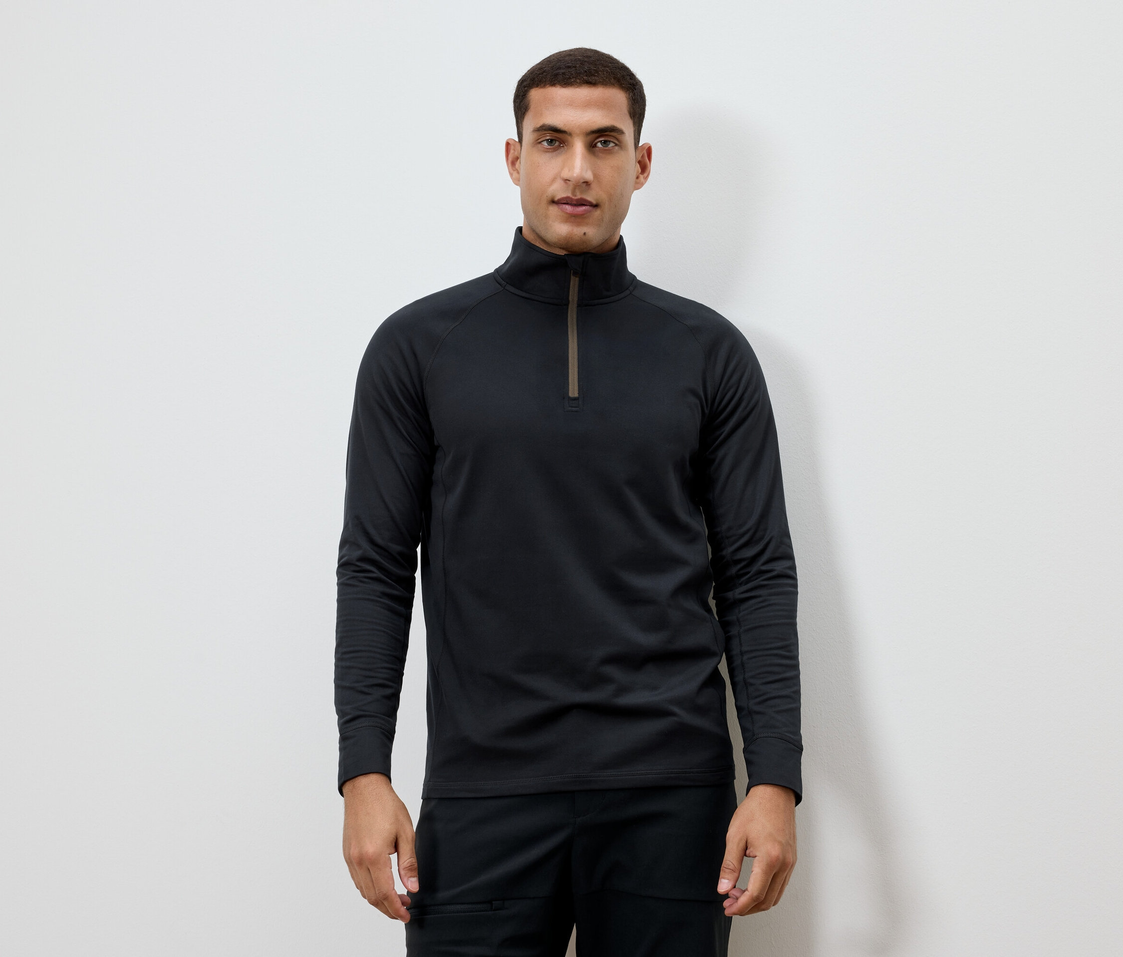 Mężczyzna ma na sobie czarną koszulkę z długim rękawem i zamkiem błyskawicznym przy szyi.