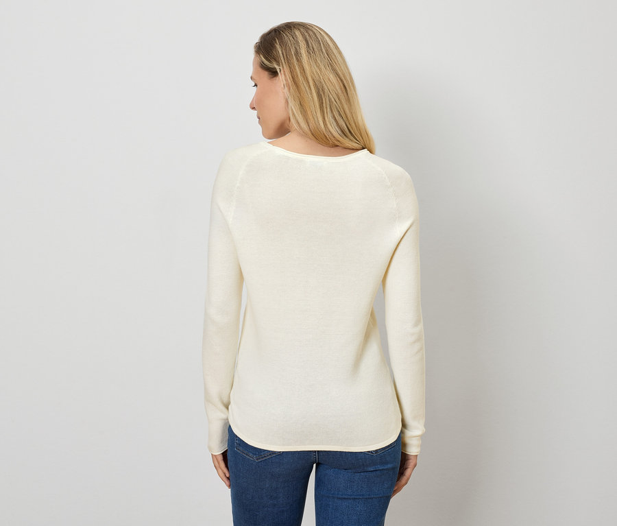 Kobieta z blond włosami stoi tyłem do kamery, ubrana w kremowy sweter i dżinsy.