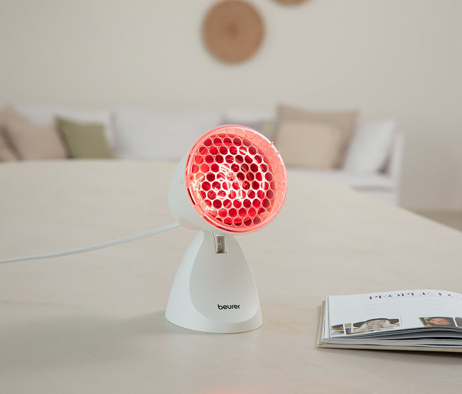 Lampa na podczerwień Beurer stoi na stole obok otwartej książki.