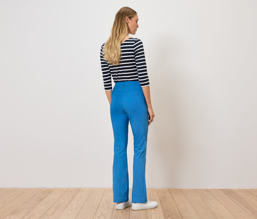 Kobieta stoi tyłem, ma na sobie niebieskie spodnie i bluzkę w paski.