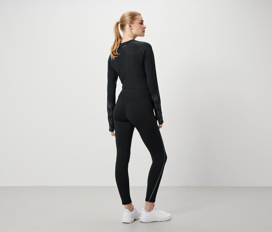 Kobieta w czarnym stroju sportowym i białych butach stoi tyłem do kamery.