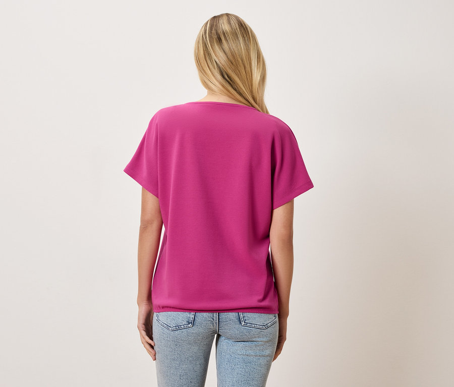 Widok z tyłu kobiety z blond włosami w różowym T-shircie i jasnoniebieskich dżinsach.