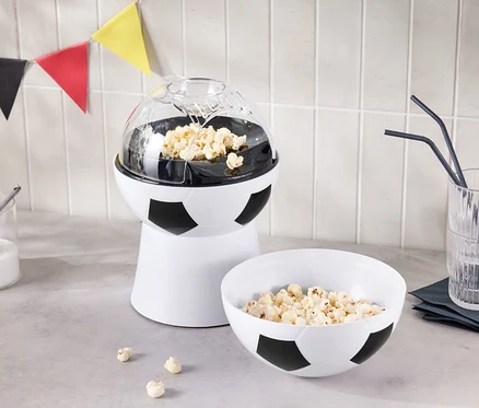 Ekspres do popcornu w kształcie piłki nożnej stoi obok miski popcornu i szklanki ze słomkami.