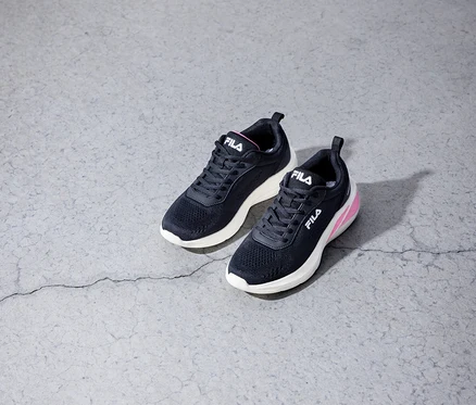 Dwa czarne sneakersy damskie FILA Specctris z białymi podeszwami i różowymi akcentami leżą na szarym betonowym podłożu.