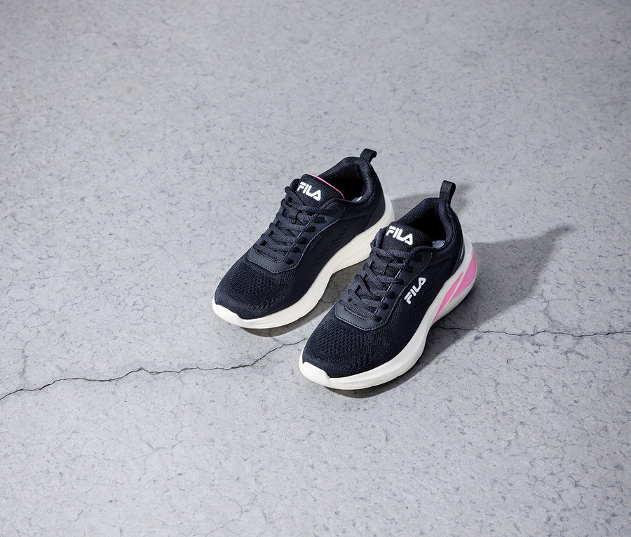 Dwa czarne sneakersy Fila leżą na szarej betonowej podłodze.