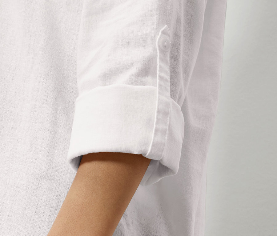 Zbliżenie na rękaw białej lnianej koszuli z podwiniętym rękawem i guzikiem.