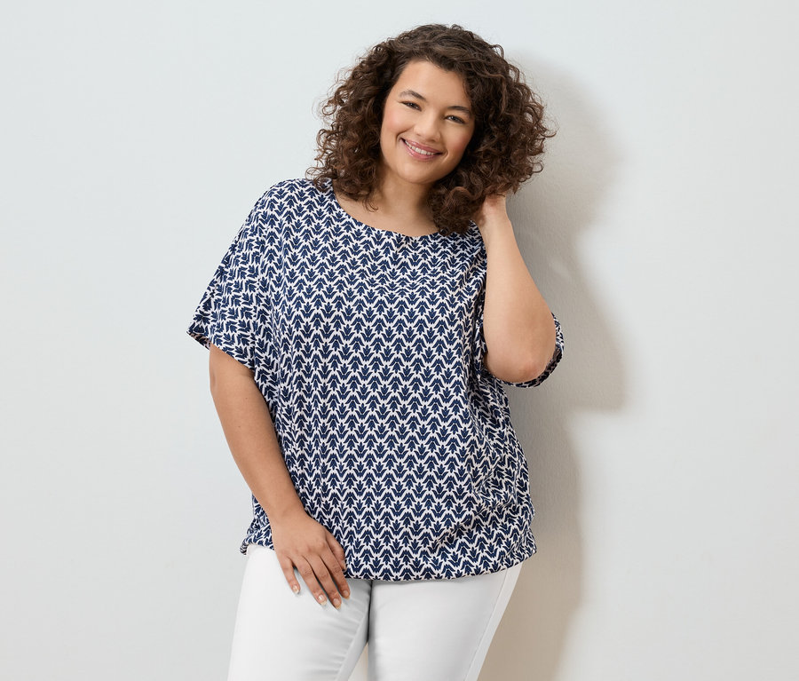 Uśmiechnięta kobieta z kręconymi włosami w biało-niebieskiej bluzce i białych spodniach.