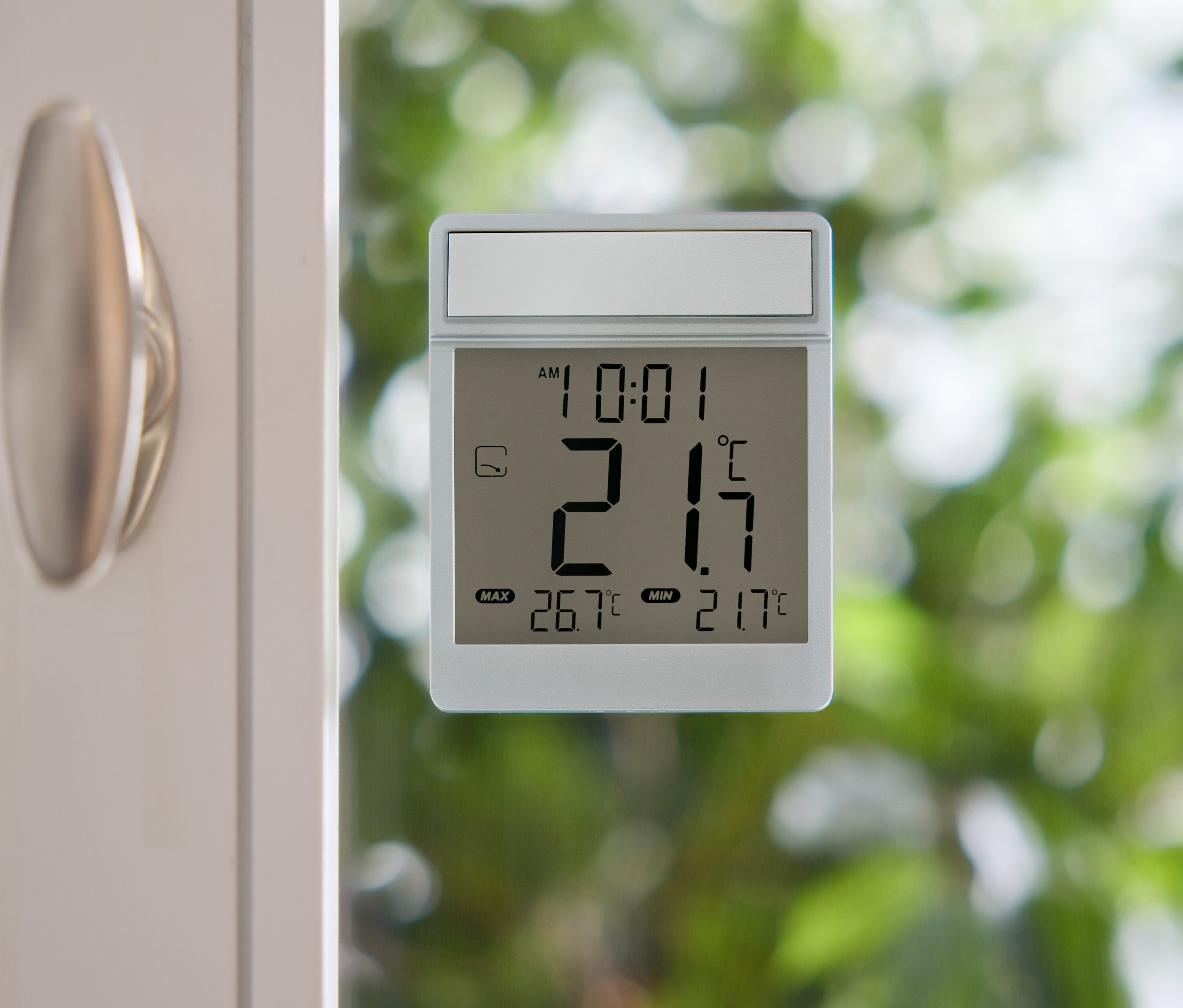 Cyfrowy termometr pokazuje 21,7 stopni Celsjusza na szybie okna.