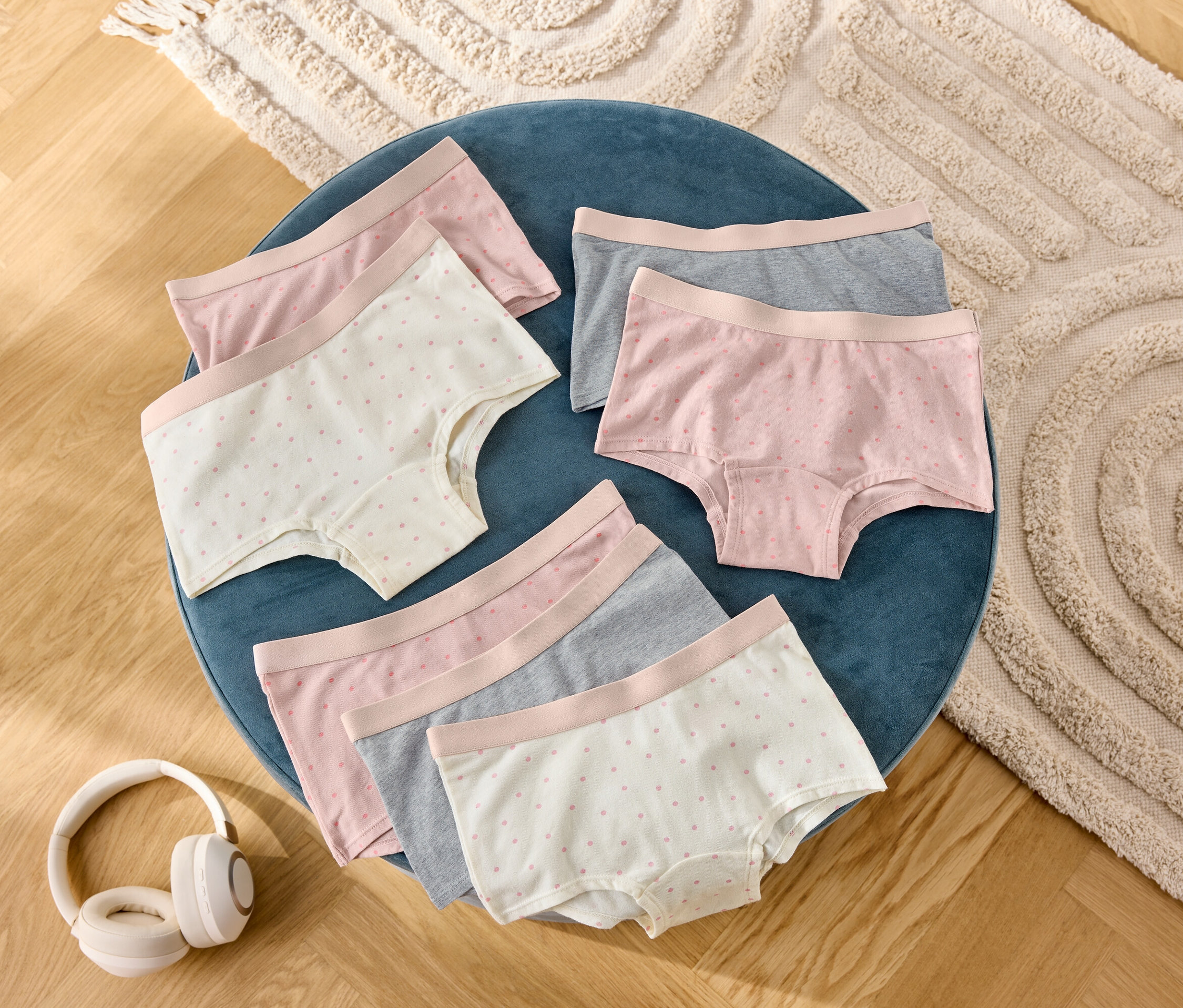Na niebieskim stołku leży sześć par damskich szortów w kolorze szarym, różowym i w kropki, obok słuchawki.