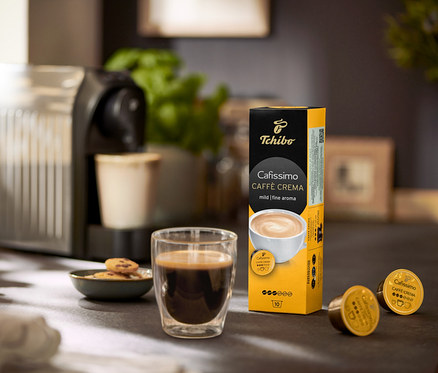 Na stole stoi ekspres do kawy, szklanka kawy i opakowanie Caffè Crema Mild – 120 kapsułek.