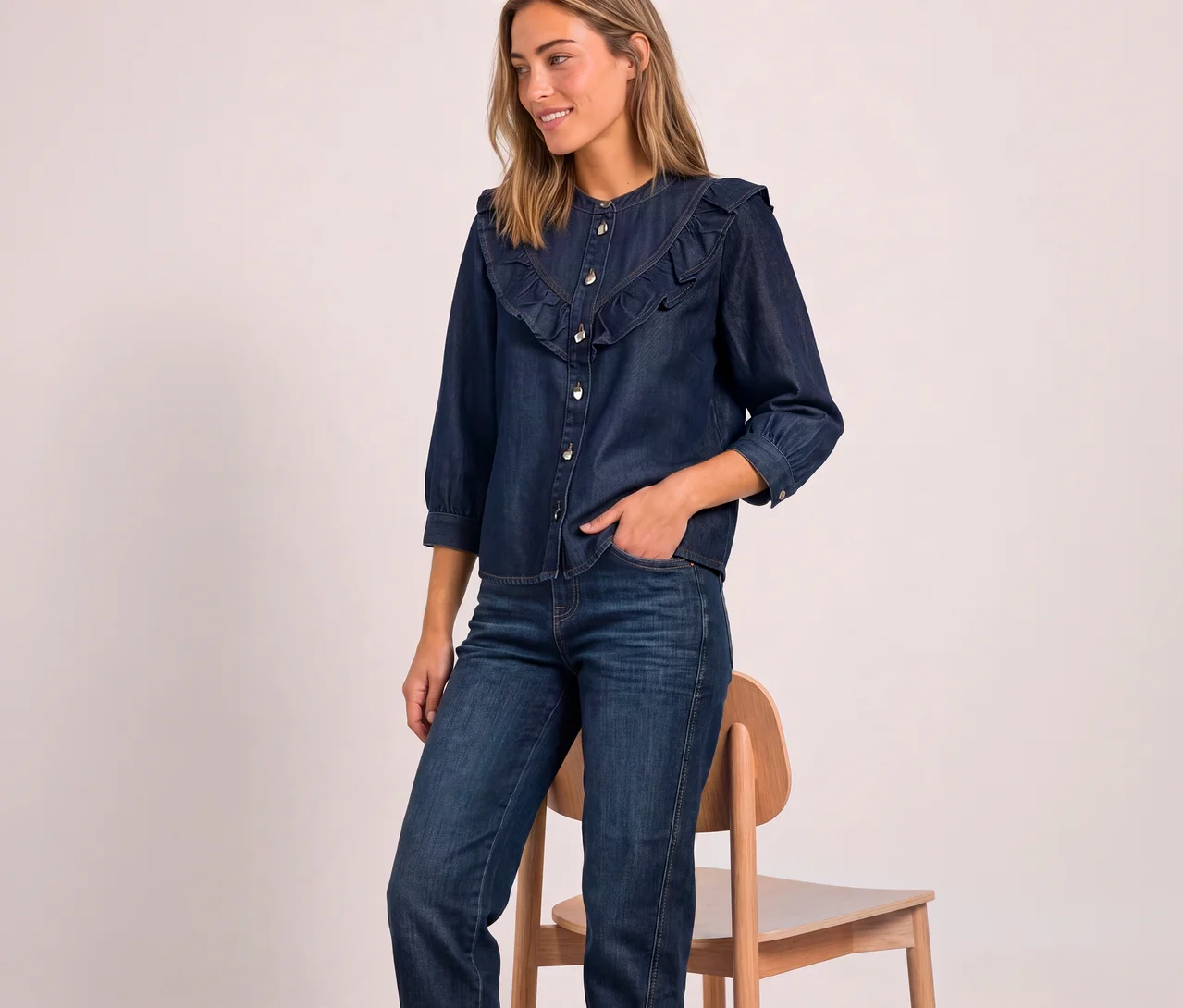 Uśmiechnięta kobieta w ciemnoniebieskiej bluzce jeansowej Street One z falbankami i rękawami 3/4 oraz w jeansach, z ręką w kieszeni.
