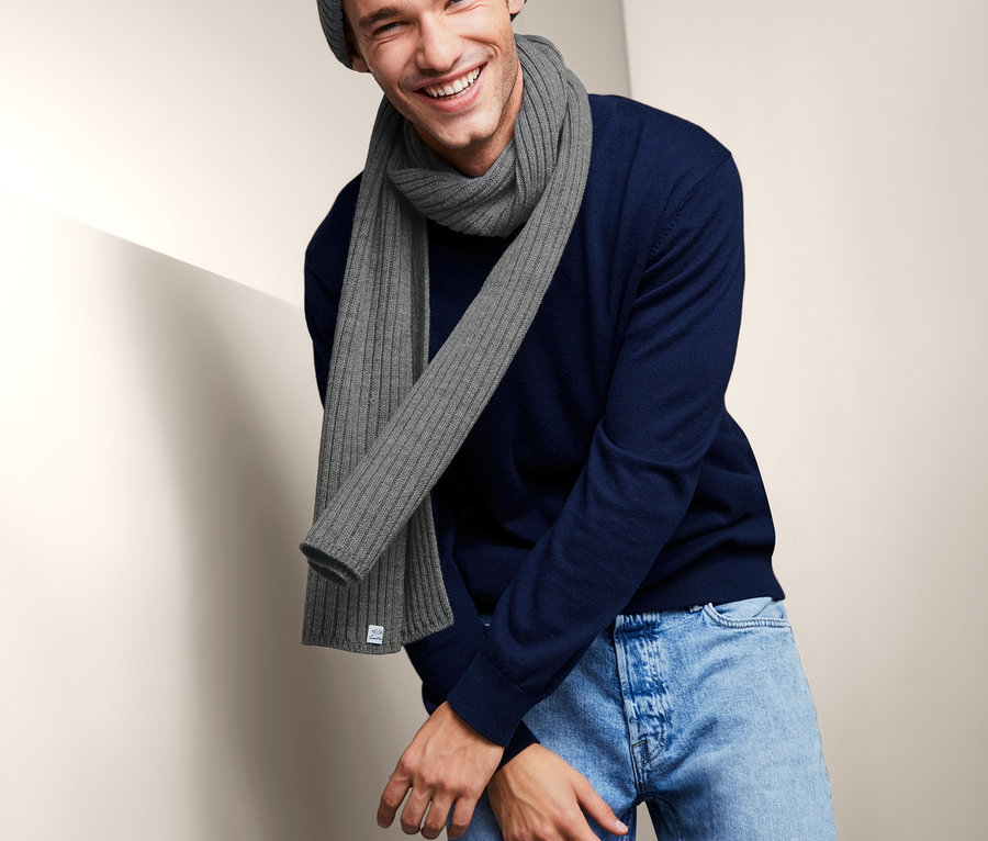 Uśmiechnięty mężczyzna w szaliku z dzianiny, czapce z dzianiny i niebieskim swetrze.