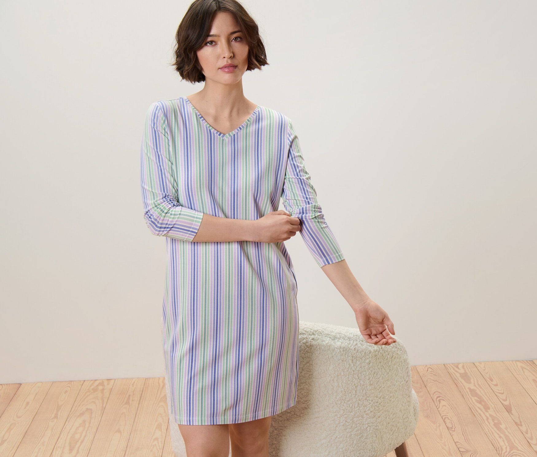 Kobieta podwija rękawy w koszuli nocnej w niebieskie, zielone i białe paski.