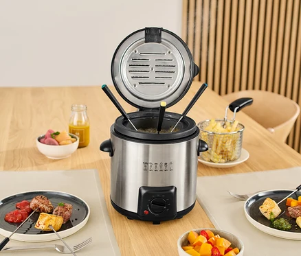 Miniaturowa frytkownica i zestaw do fondue na stole z jedzeniem na talerzach i w miskach.