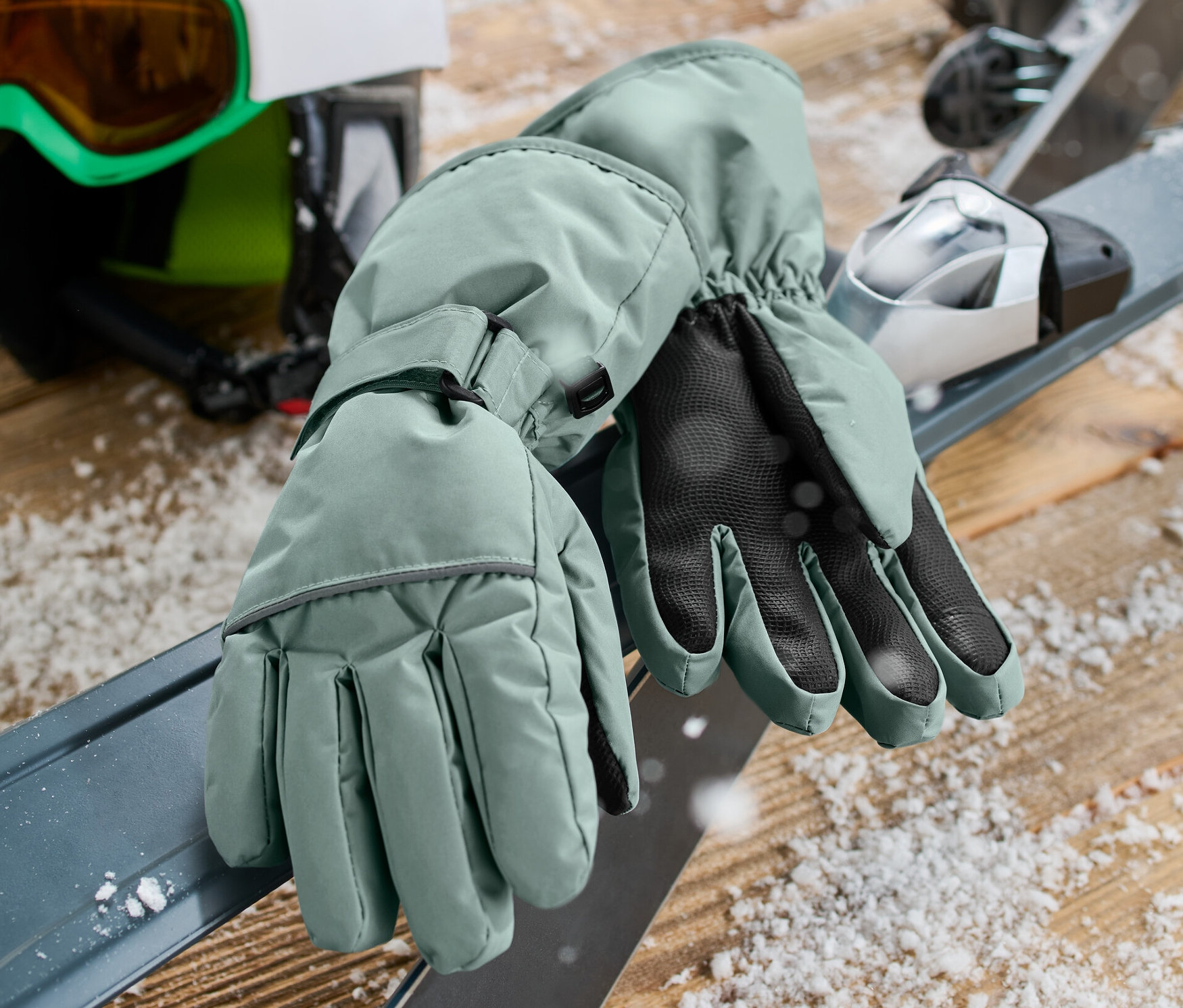 Zielone dziecięce rękawiczki narciarsko-zimowe leżą na nartach obok kasku i gogli.