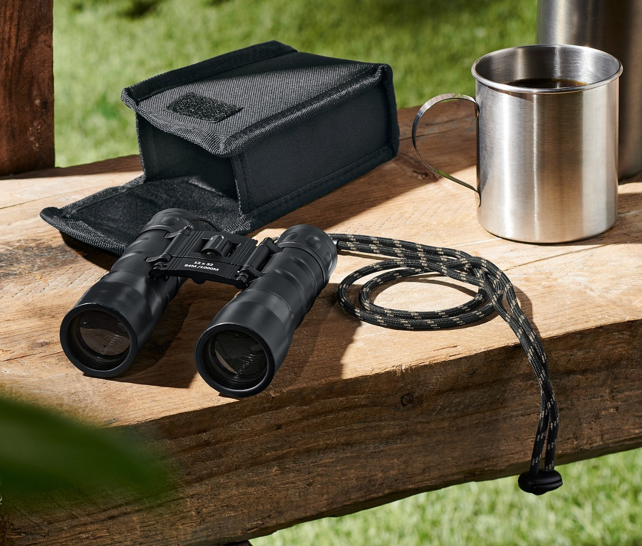 Lornetka kieszonkowa »12x32« leży obok etui, termosu i kubka na drewnianej ławce.