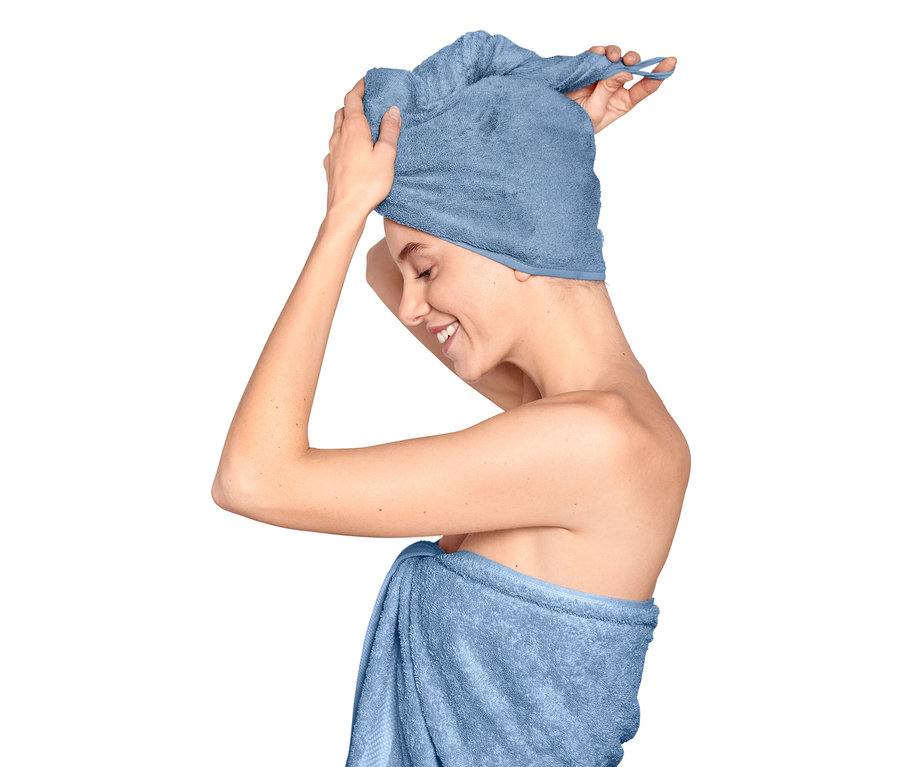 Kobieta poprawia ręcznik-turban na głowie, ciało owinięte ręcznikiem.