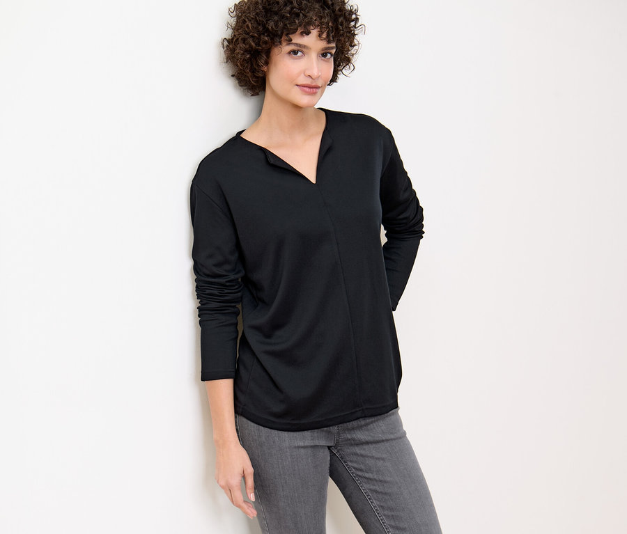 Kobieta oparta o ścianę ma na sobie czarną bluzkę.